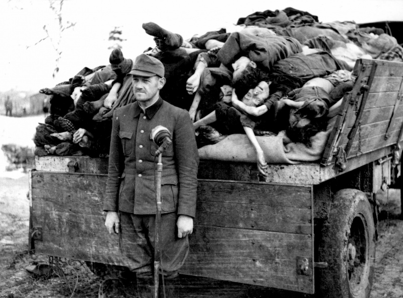 Бывший оберштурмфюрер СС Франц Хёсслер (Franz Hößler, 1906—1945) у микрофона перед грузовиком с телами узников концлагеря Берген-Бельзен.